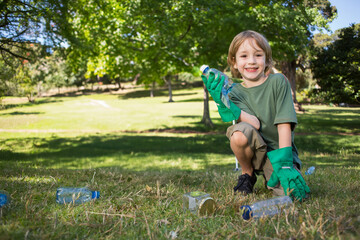 Boy wearing green gloves kneeling and picking up bottles and glass jar at park, copy space