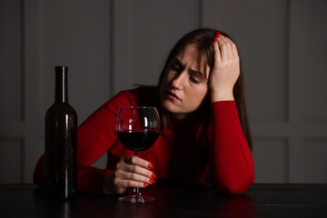 Alcohol addiction. Woman with glass of red wine and bottle at wooden table indoors