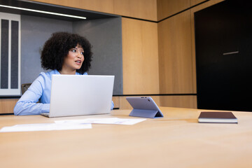 African American woman in blue blouse reviewing papers on laptop at meeting table, copy space