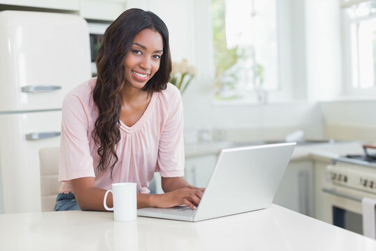African American woman typing on silver laptop at white kitchen island near ceramic mug and flowers
