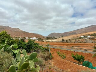 The view of a typical farm "finca" in Fuerteventura island, Canary Islands, Spain, red volcanic soil and mountains, cloudy weather