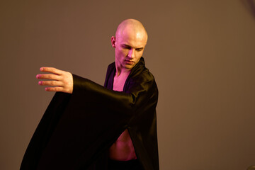 Engaging man in a flowing black robe showcases movement and grace in a captivating light setting, emphasizing his artistic expression.