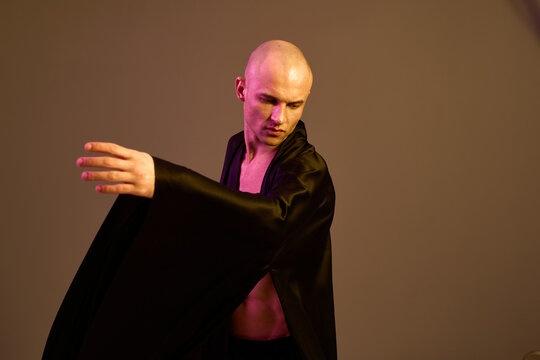 Engaging man in a flowing black robe showcases movement and grace in a captivating light setting, emphasizing his artistic expression.