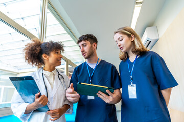 Medical team discussing patient's diagnosis using tablet and x ray in hospital corridor