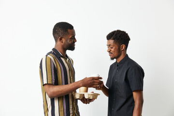 Two smiling black men sharing a coffee moment, dressed casually in stylish attire, creating a warm and friendly atmosphere together.