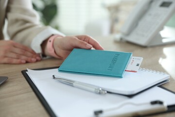 Travel agent with passport and ticket at wooden table in office, closeup
