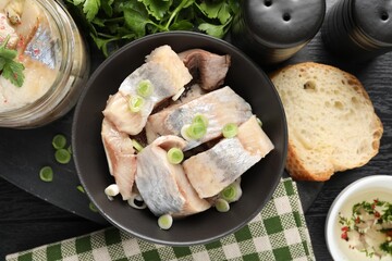 Pieces of delicious herring with green onions on black wooden table, flat lay
