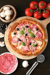 Tasty pizza, ingredients and cutter on black wooden table, flat lay