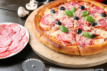 Tasty pizza, ingredients and cutter on black wooden table, closeup