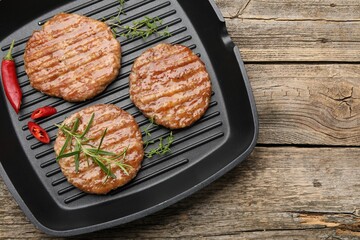 Delicious hamburger patties and spices in frying pan on wooden table, top view. Space for text