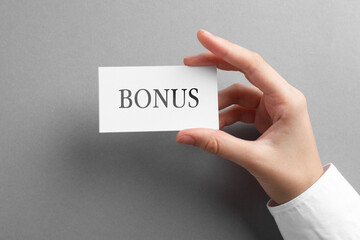 Woman holding card with word Bonus at grey table, top view