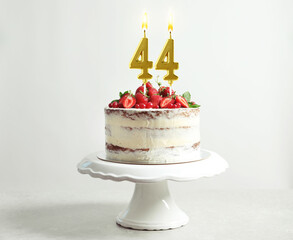 Yummy cake with fruits and burning number shaped candles on white background. 44th birthday or...