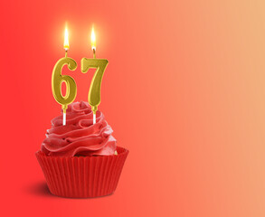 Yummy cupcake with burning number shaped candles on red gradient background, space for text. 67th birthday or other special occasion
