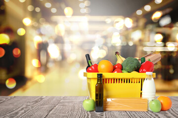 Yellow shopping basket with groceries on wooden table in supermarket. Space for text