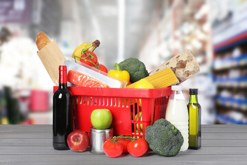 Red shopping basket with groceries on wooden table in supermarket