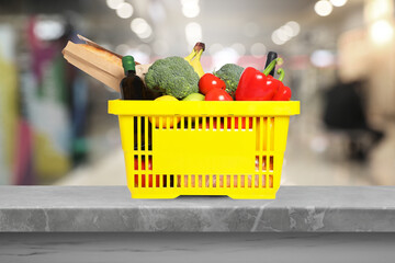 Yellow shopping basket full of groceries on grey table in supermarket