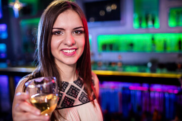 Wine glass reflecting green and blue LED lights standing on bar top with illuminated shelves