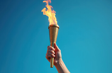 Hand holding Olympic flame against blue sky. Symbol of international sports games. Gold torch with burning flame, victory achievement concept. Success sports games, competition event winner