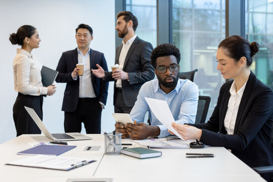Diverse business team collaborating in a modern office setting, focusing on documents and technology for their project.