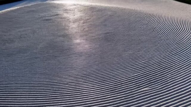 A close-up view of a textured, undulating surface.  Parallel, wavy lines create a sense of depth and motion. Sunlight glints off the surface