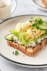 Scrambled eggs on grilled toast with salad leaves, cheese and micro greens on plate. Delicious breakfast or brunch close up
