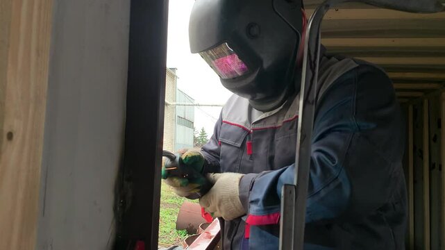 The welder works with a welding machine. A builder uses a welding machine to make a window frame.