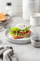 Toasted bread with poached egg, salad, cheese and ham on a plate on white kitchen background. Healthy breakfast, diet food