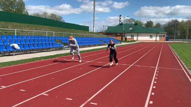Father and daughter are running around the stadium. A man is racing with a girl.