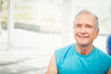 Senior man standing in sunroom wearing blue athletic shirt and smiling toward camera, copy space