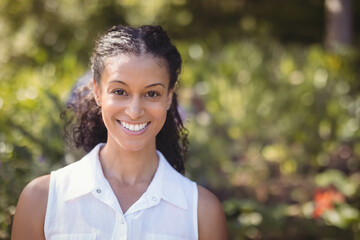 African American woman standing and smiling in sunlit garden wearing sleeveless collared shirt