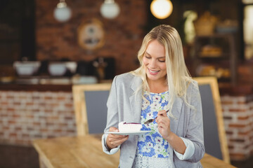 Twenty-something woman wearing floral dress and blazer holding cake slice on ceramic plate at cafe