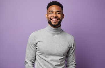 Obraz premium Happy young black man on purple background. Smiling male with beard in grey turtleneck. Cheerful person expresses positive emotion. Portrait of attractive modern guy.