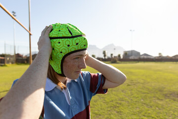 Teenage female athlete wearing rugby jersey pulling neon green scrum cap on rugby field, copy space