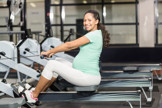 African American pregnant woman pulling cable rower handle while sitting on sliding seat in gym