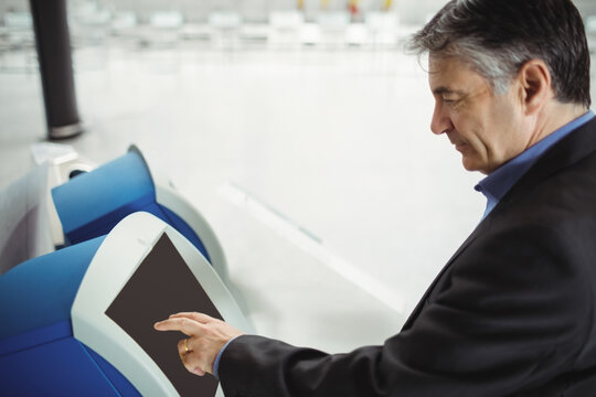 Businessman pressing touchscreen on blue-and-white check-in kiosk in airport terminal, copy space