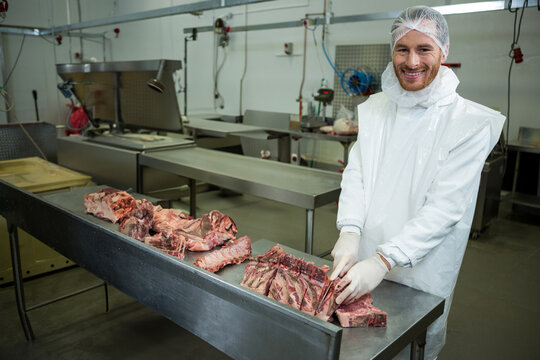 Male worker wearing uniform holding knife at processing plant with meat cuts, copy space