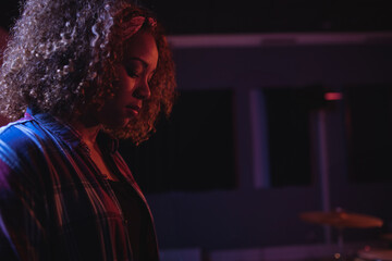 Woman standing under purple and red stage lighting in music studio with drum cymbal