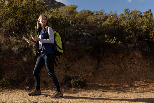 Folded paper map resting on trail near scrub-covered hill, with neon green backpack and smartphone