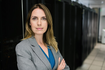Woman wearing blazer standing arms crossed among server racks in data center corridor, copy space