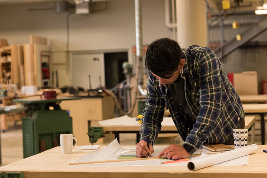 Drafting plans and coffee mug are lying on large wooden workbench in carpentry workshop among tools