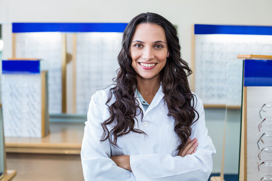 Female optical specialist wearing lab coat examining eyeglass frames on wooden counters in showroom