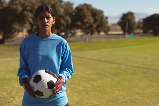 Asian woman goalkeeper standing on soccer field holding ball by goalpost wearing gloves, copy space