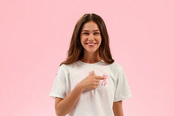 Smiling young woman pointing at pink ribbon on t-shirt, breast cancer awareness and support concept