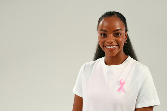 Smiling African American woman wearing pink ribbon, breast cancer awareness and support concept