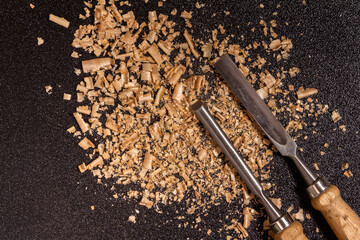 two wooden-handle chisel with wooden chips and sawdust on a black speckled background top view
