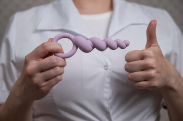 Woman in doctor's coat holding anal beads. 