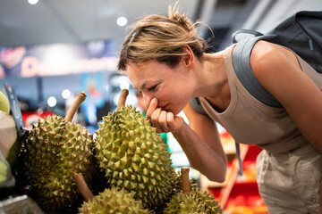 Disgusted woman wrinkles pinch nose while sniffing durian fruit on market counter. Facial reaction,...