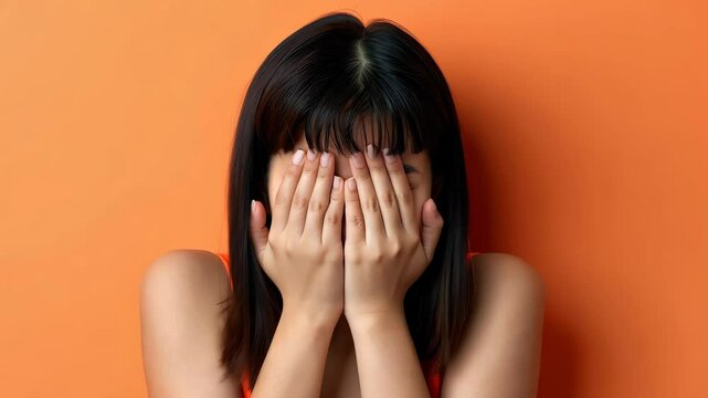 Hidden Emotions: A woman closes her eyes and covers her face, conveying a spectrum of complex human feelings like embarrassment or fear, in a compelling studio portrait.