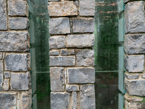 A brick wall with a narrow glass window in the middle. The wall is grey and the window is clear.