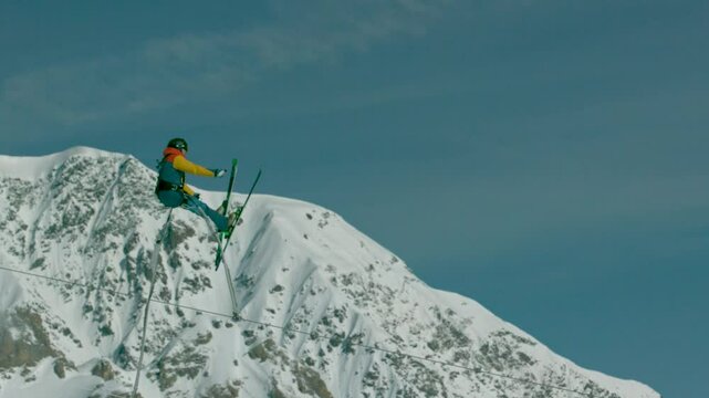 Bungee jumper on skis leaping off tall ramp in beautiful snowy mountains in super slow motion